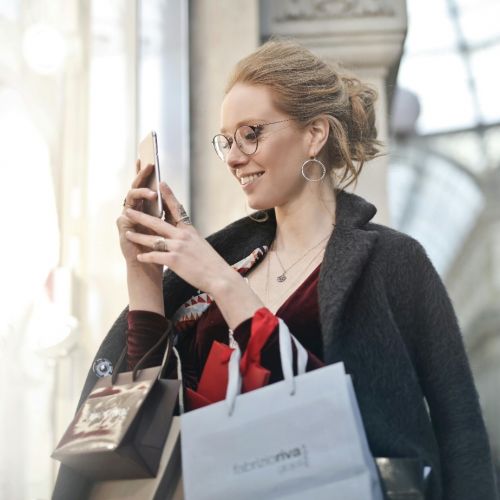 Une femme souriante faisant les soldes d’hiver, smartphone à la main