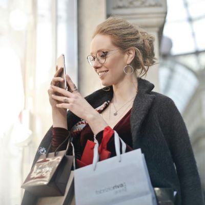 Une femme souriante faisant les soldes d’hiver, smartphone à la main