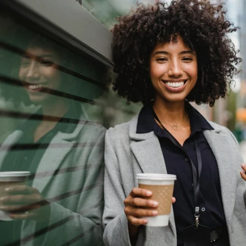 Une femme souriante tenant un smartphone et un café
