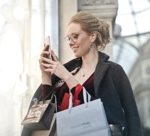 Une femme souriante faisant les soldes d’hiver, smartphone à la main